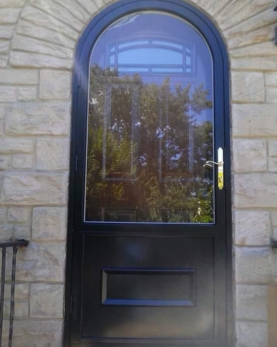 Black arched storm door with glass and brass hardware on stone masonry