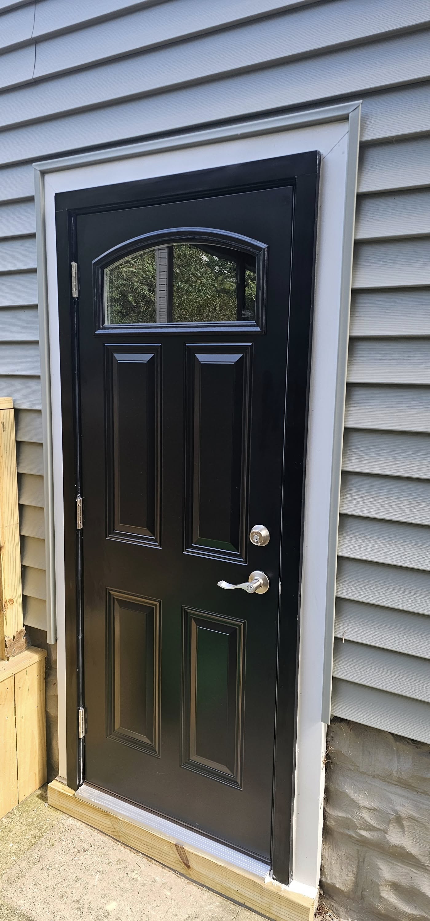 Black entry door with arched window and silver hardware on gray lap siding