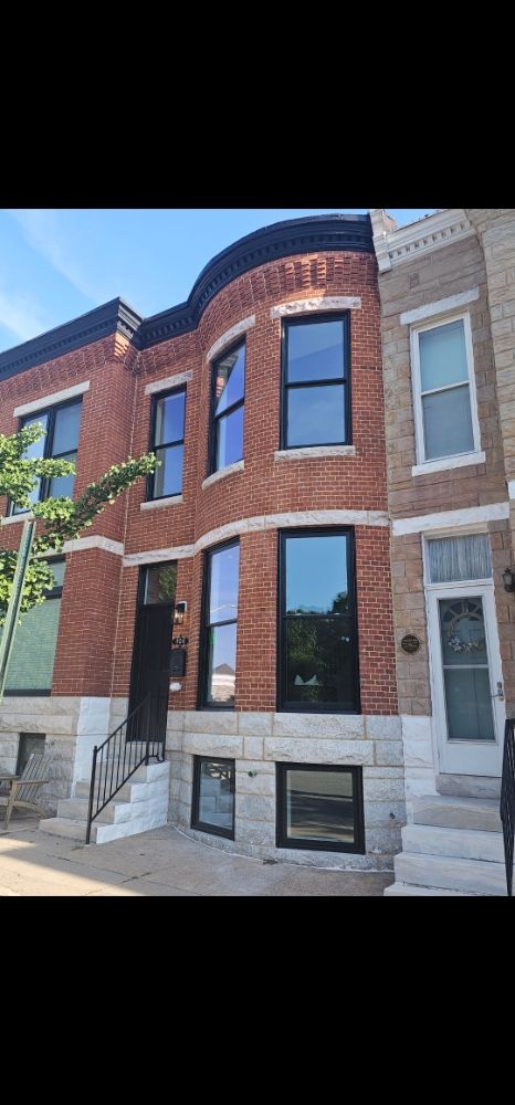 Black-framed double-hung windows and matching black front door with transom on a red brick rowhouse with a curved bay