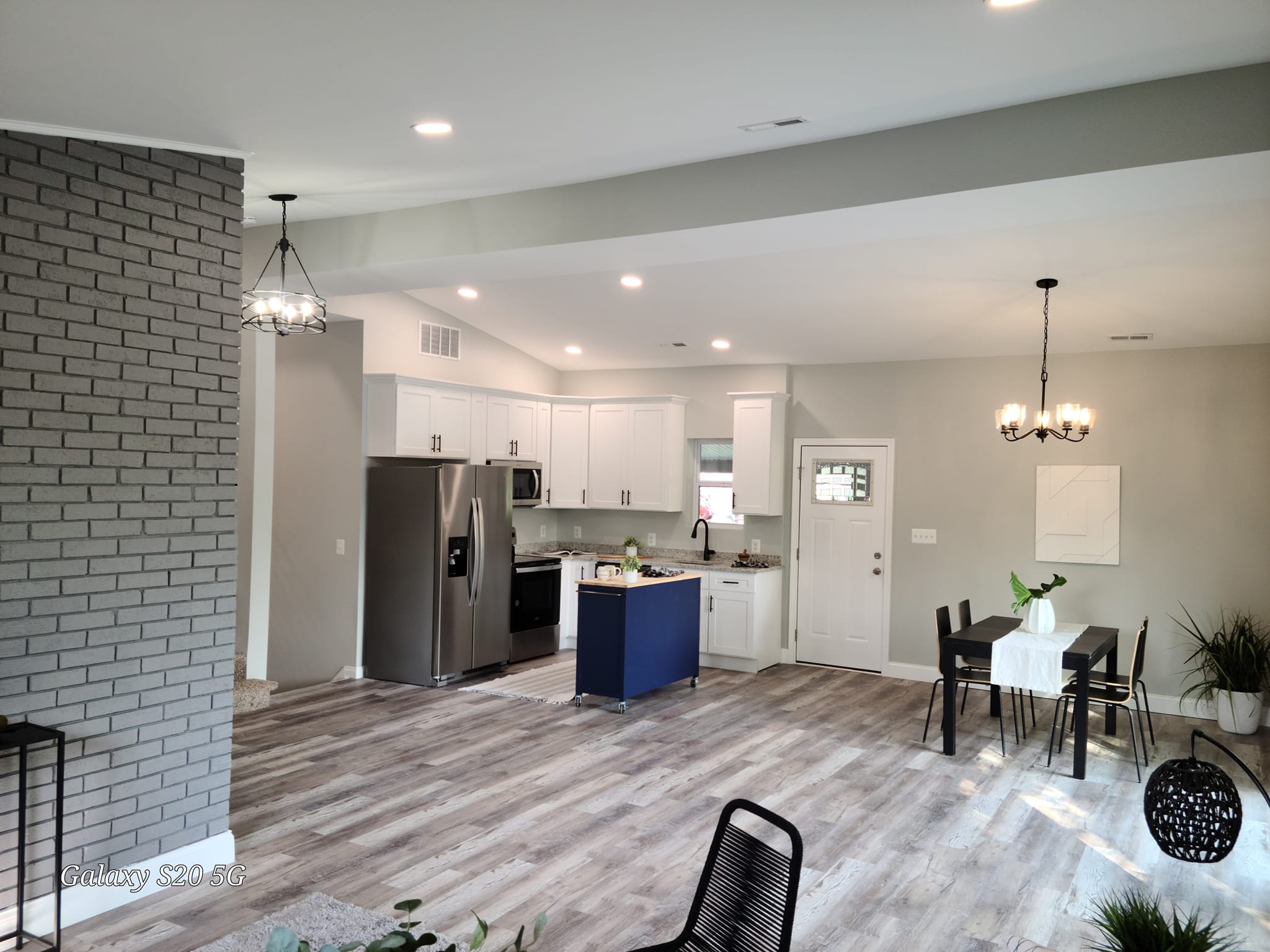 Renovated open kitchen and dining with white cabinets and grey painted brick accent wall