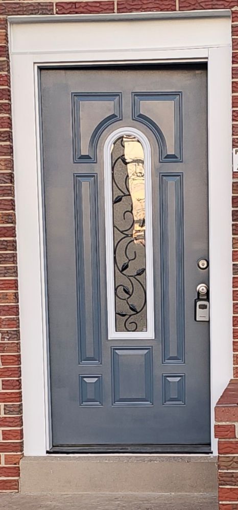 Slate blue front entry door with arched decorative glass and wrought iron detail on a red brick home