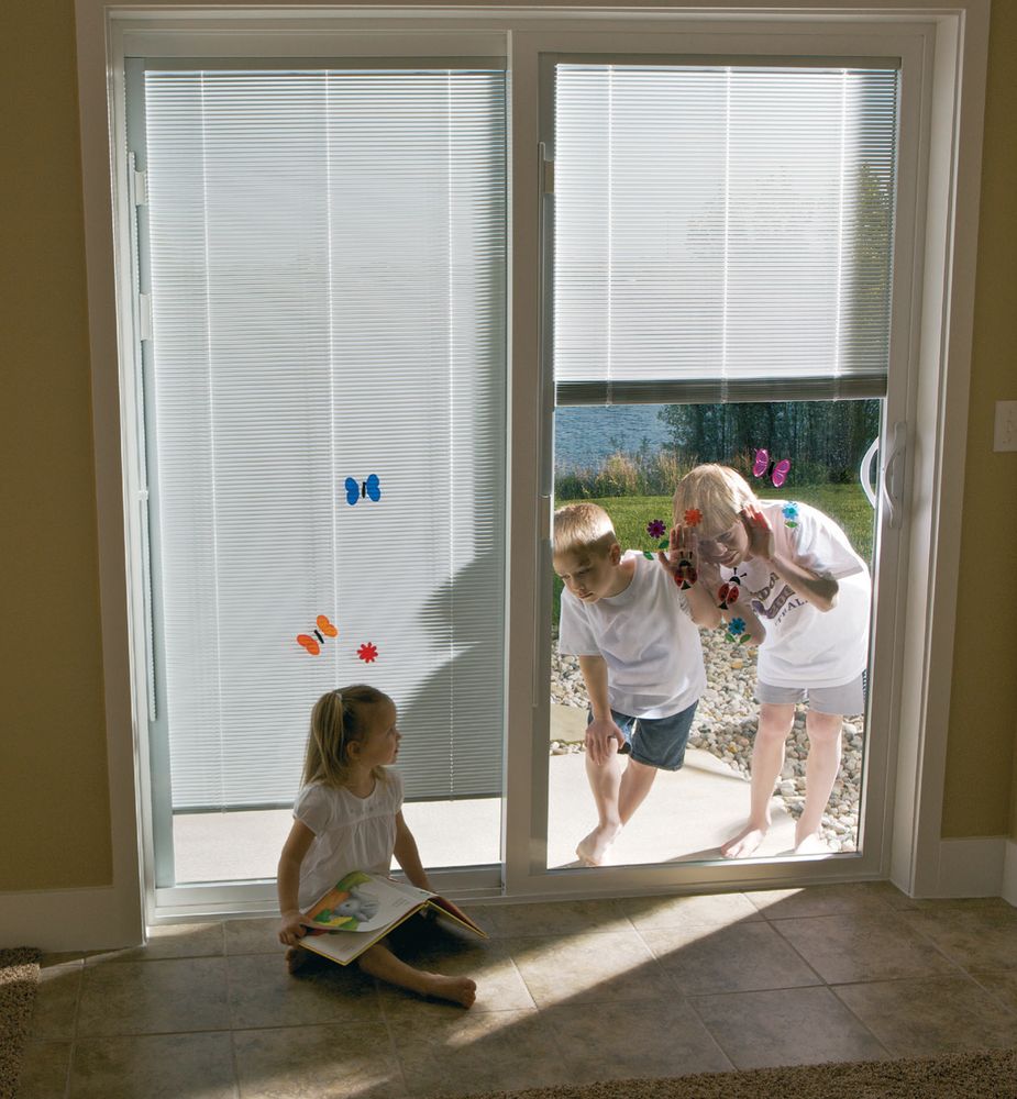 White sliding glass patio door with blinds between the glass; interior view toward a sunny backyard and lake