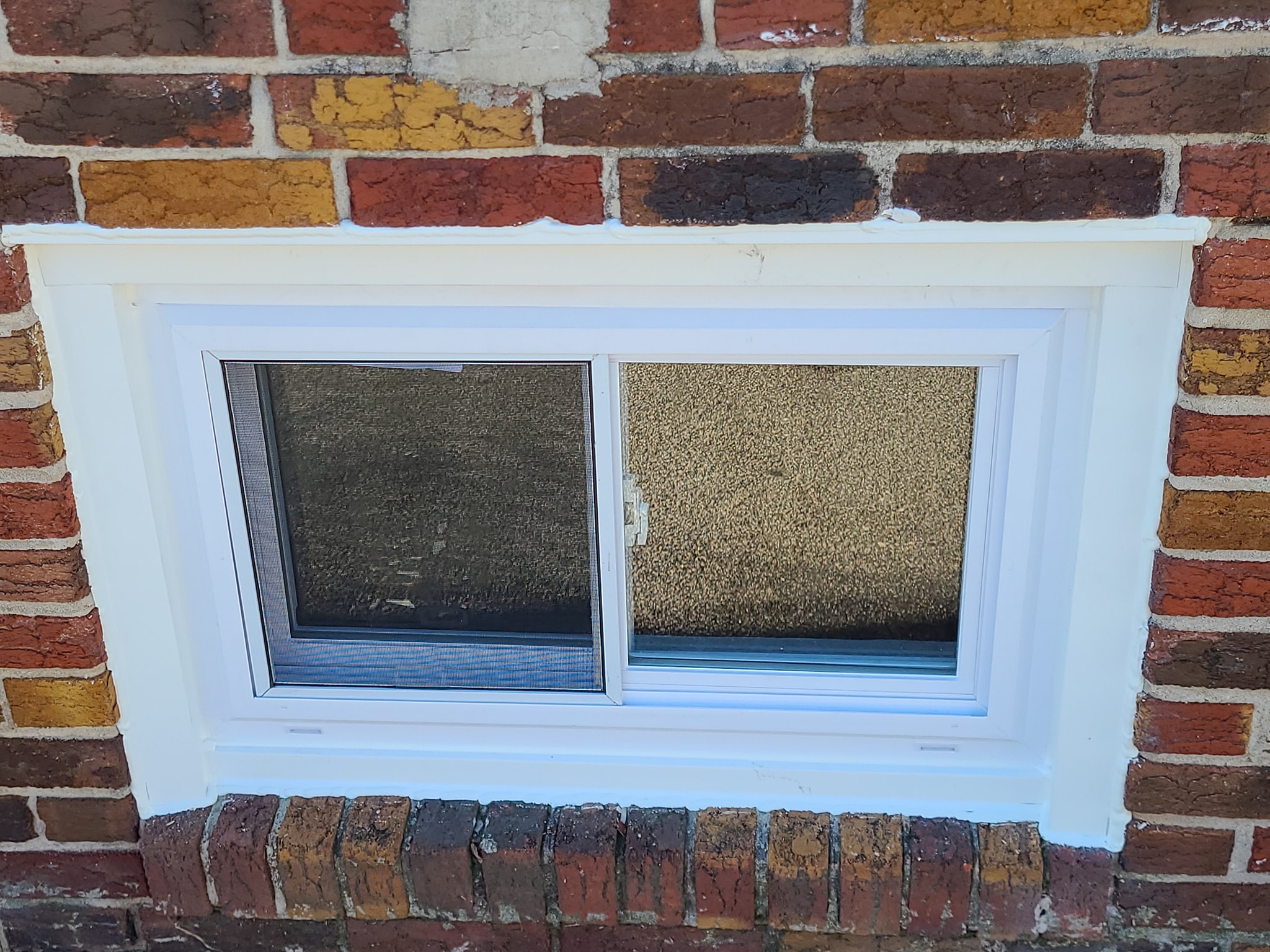 White horizontal sliding basement window with privacy glass in red brick