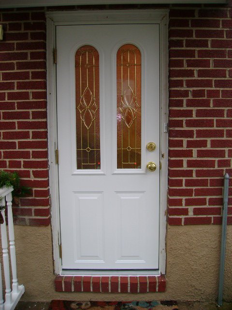 White entry door with two arched decorative glass panels and brass hardware on a red brick house