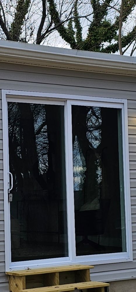 White sliding glass patio door on gray horizontal siding with wood steps to the threshold