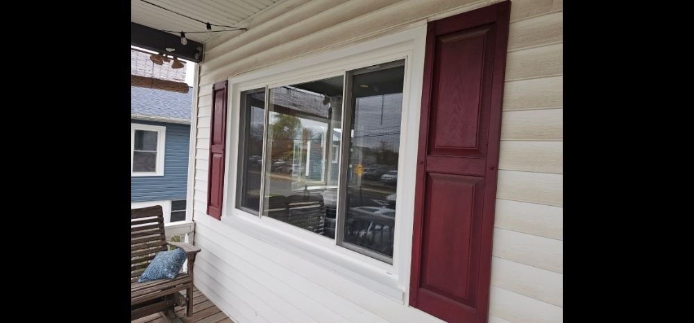 Large white three-pane horizontal sliding window with burgundy shutters on cream lap siding
